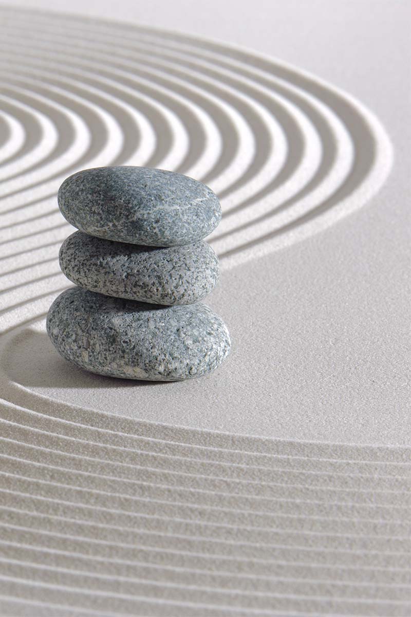 3 grey stones stacked in a column, on sand with swirl pattern